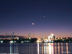 Imagem do trio brillhante de planetas (Vênus, Mercúrio e Marte) juntamente com a Lua nova acima das luzes coloridas da cidade na Austrália. <br /> <br /> Palavras-chave: Astronomia, gravitação universal, planetas, Lua, Terra, Vênus, Mercúrio, Marte, luz, reflexão.